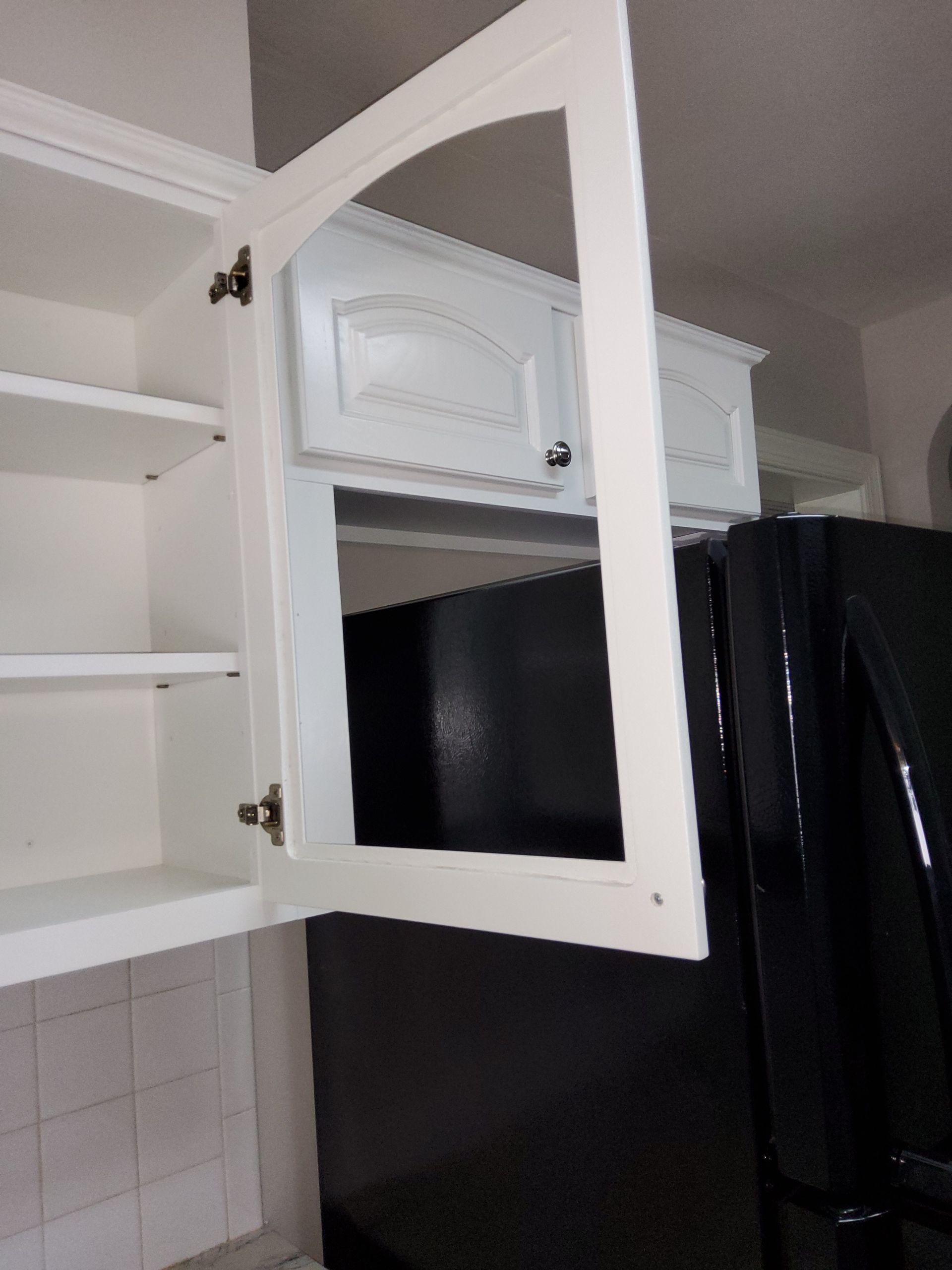 A kitchen with white cabinets and a black refrigerator