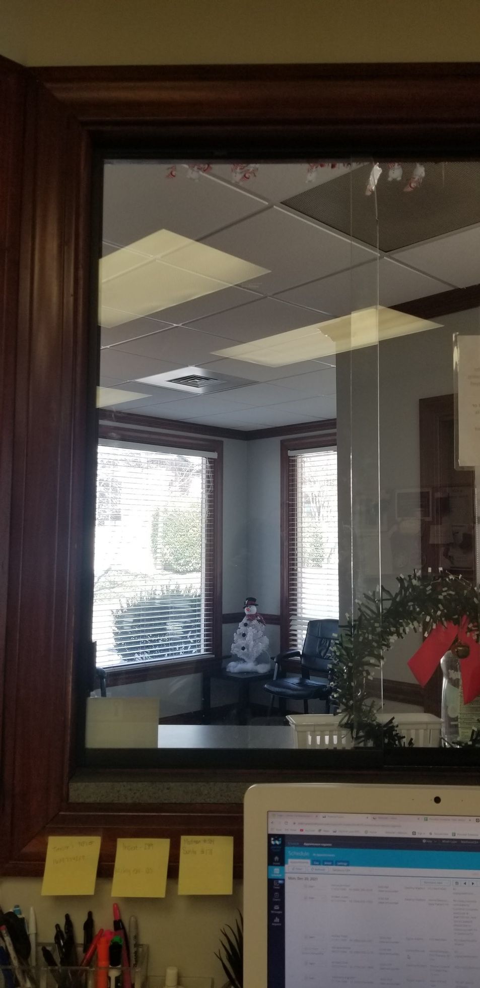 A computer is sitting on a desk in front of a window in an office.