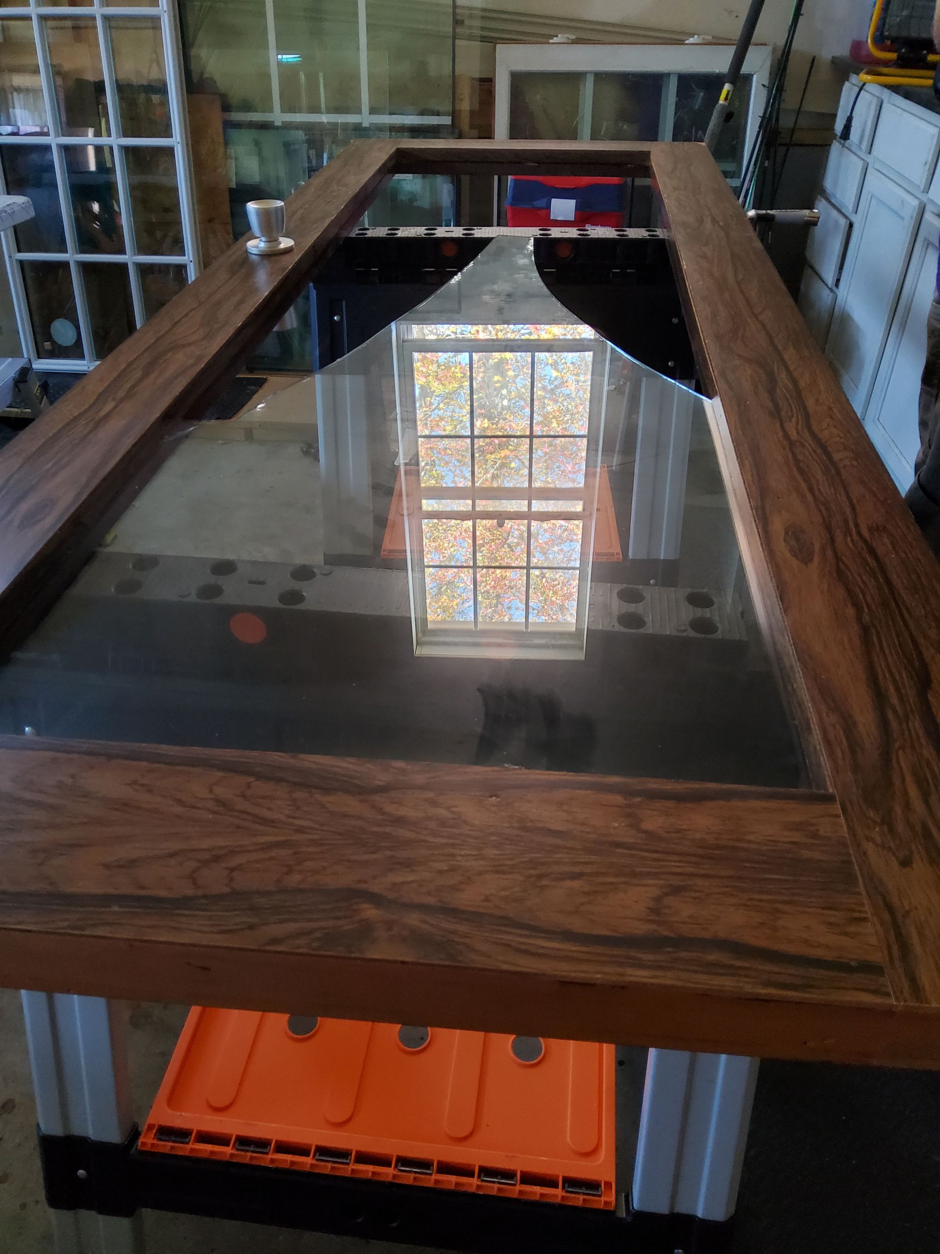 A wooden table with a glass top and a reflection of a window