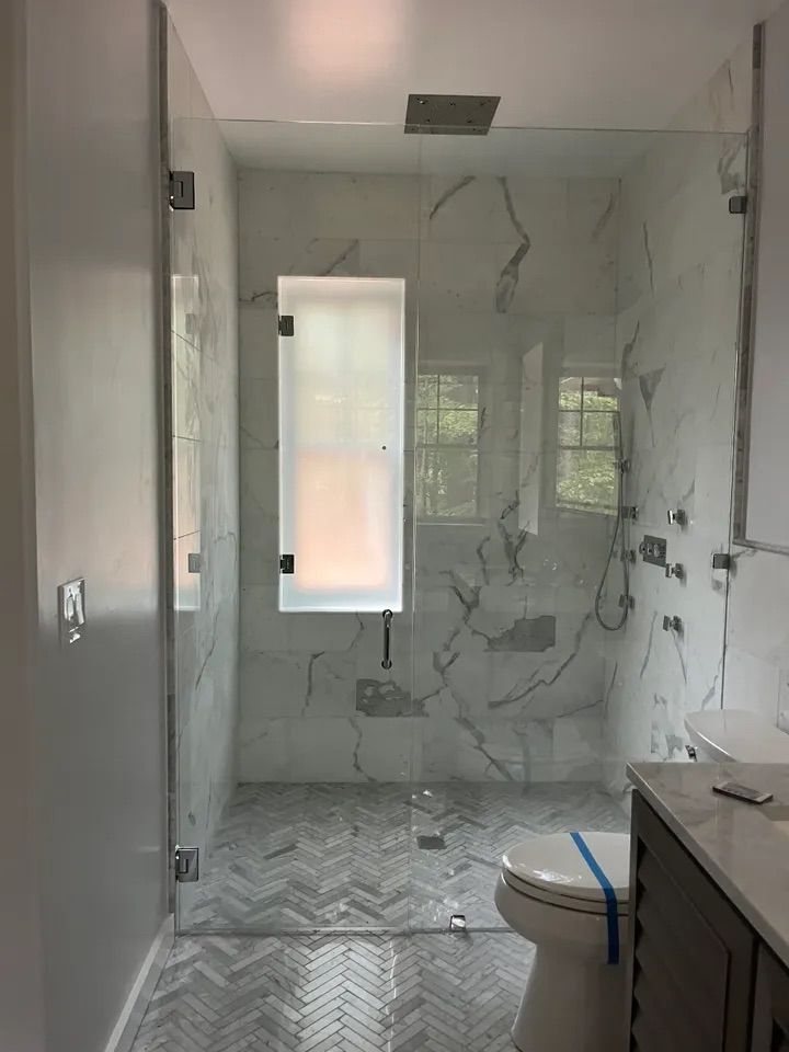 A bathroom with a walk in shower , toilet , sink and window.