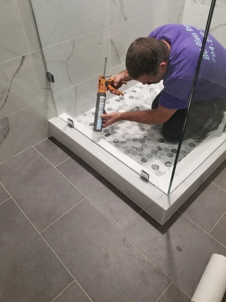 A man in a purple shirt is installing a shower door in a bathroom.