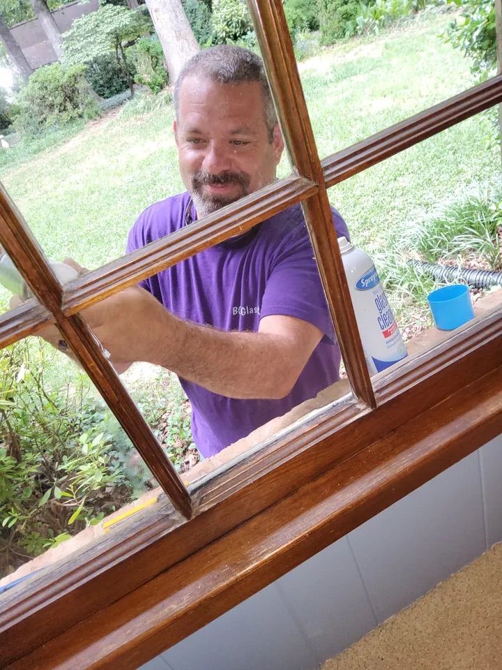 A man in a purple shirt is cleaning a window.
