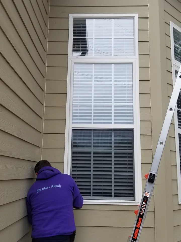 A man in a purple jacket is working on a window