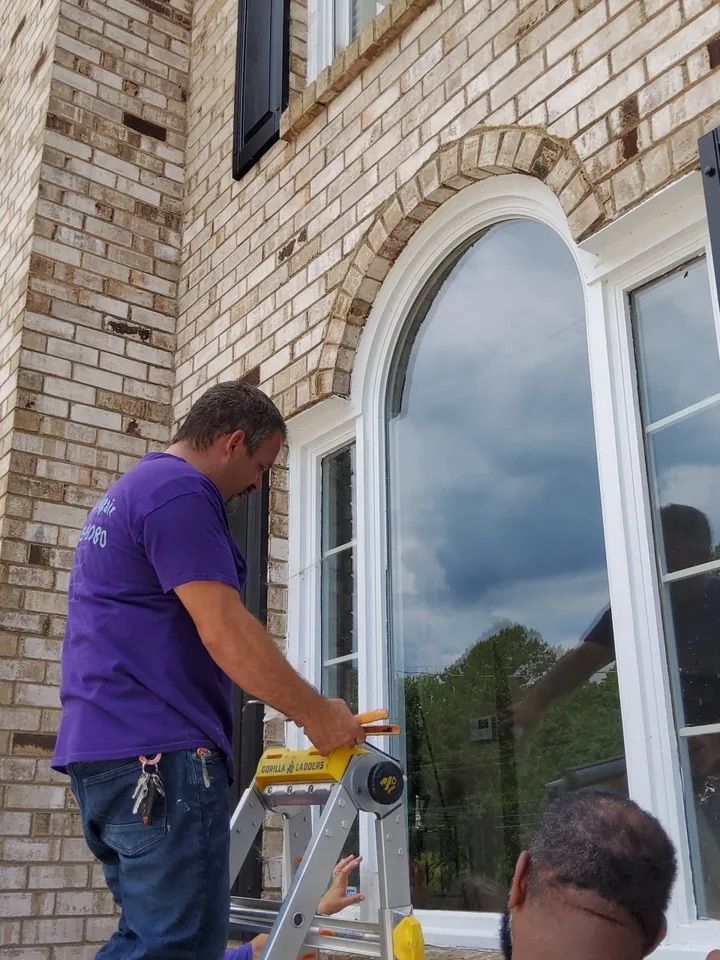 A man in a purple shirt is standing on a ladder in front of a brick building.