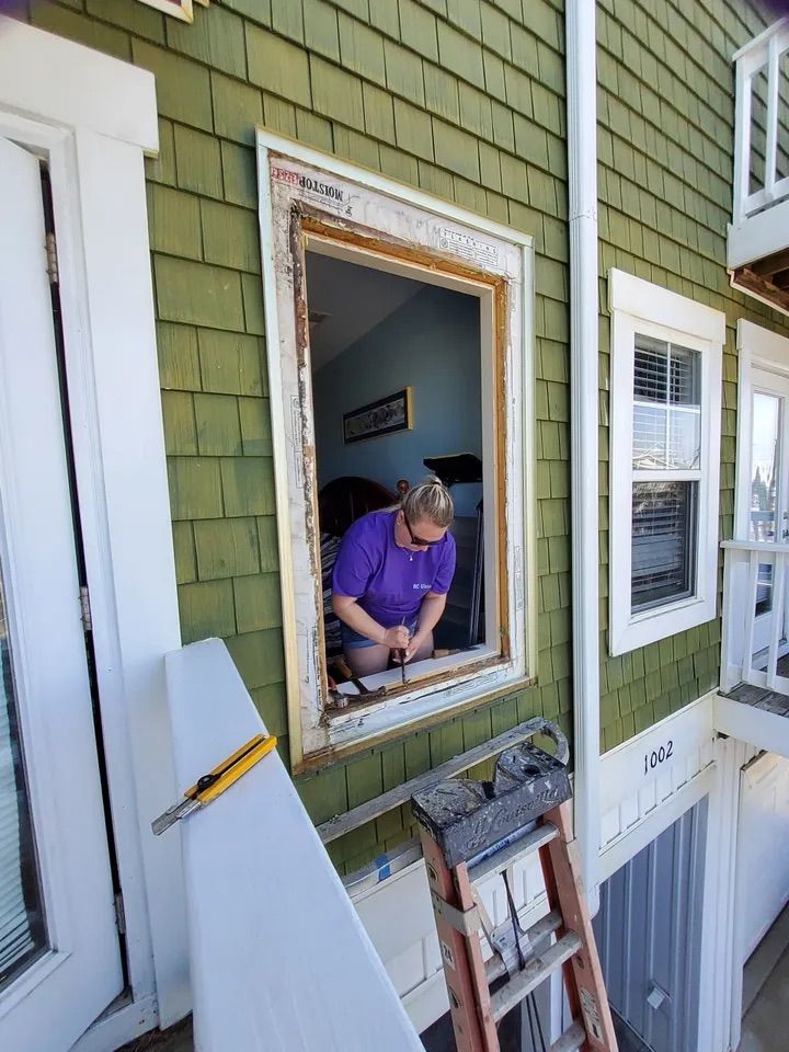 A man is working on a window on the side of a house.