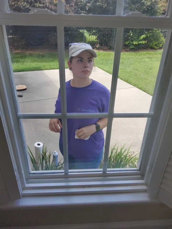 A woman in a purple shirt is cleaning a window.