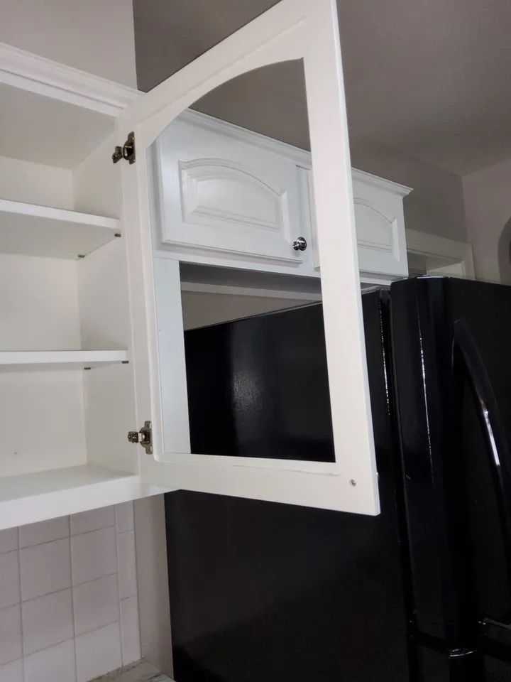A kitchen with white cabinets and a black refrigerator