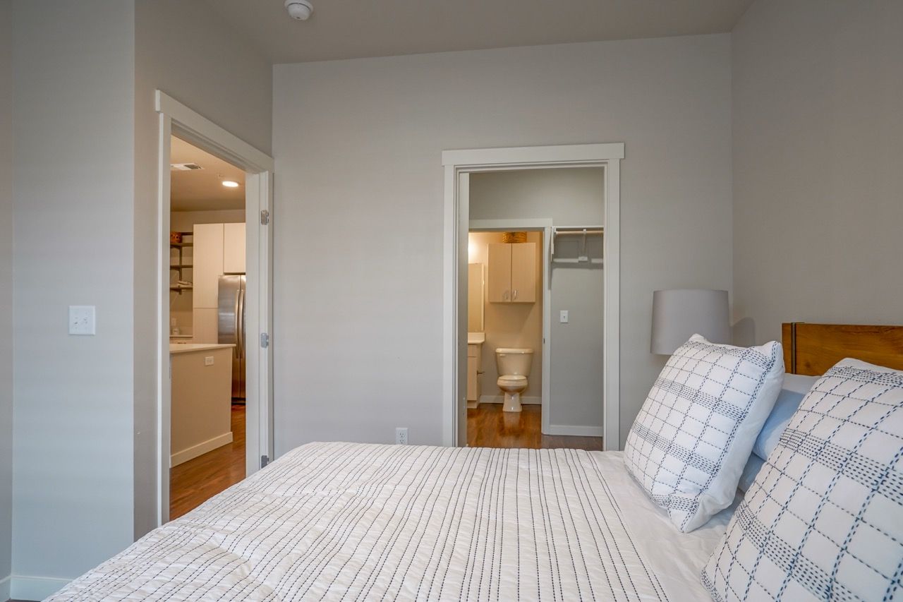Bedroom interior with a bed; doorway to an adjacent bathroom and a visible kitchen.