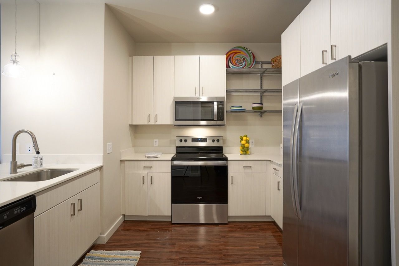 Modern apartment kitchen with white cabinets, stainless fridge, stove, and microwave