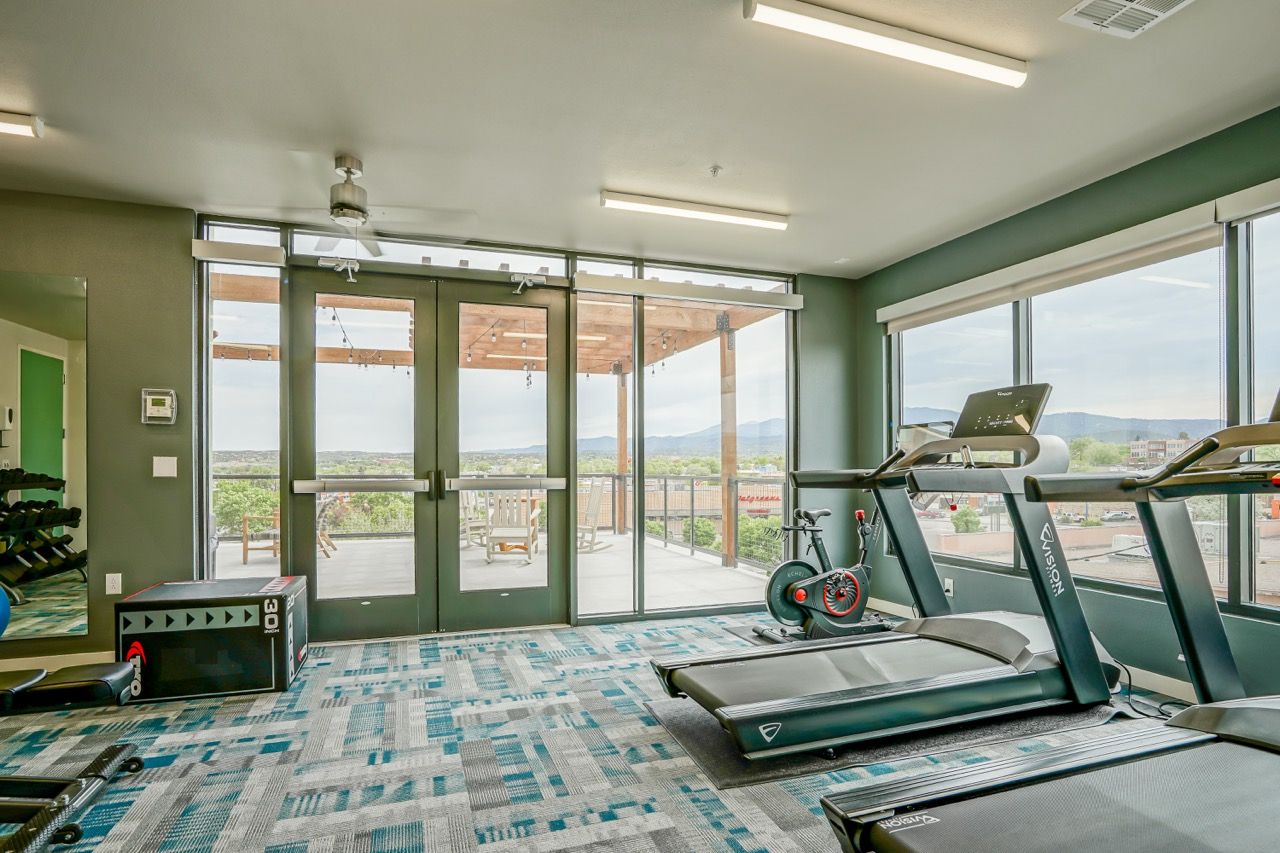 Modern fitness center with treadmills and a cycling bike near large glass doors to an outdoor balcony.