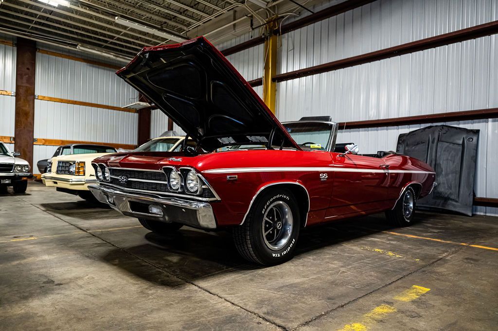 Red classic convertible car with open hood, inside a garage.