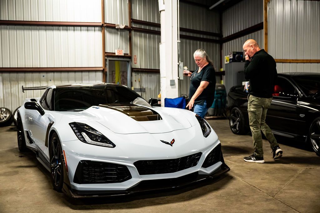 White Corvette in a garage; two people look at the car.