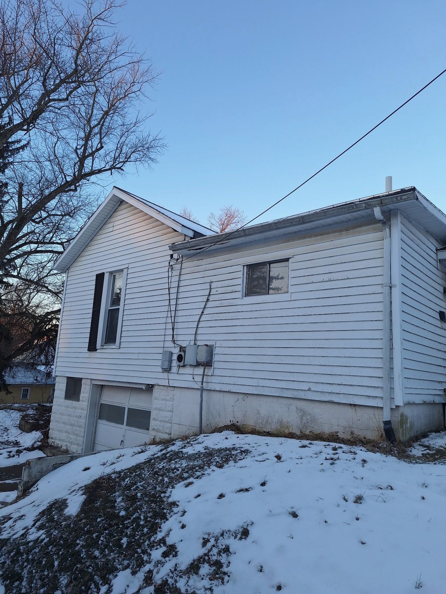 A white house with wood-style siding, a small garage, and a snowy yard under a clear blue sky.