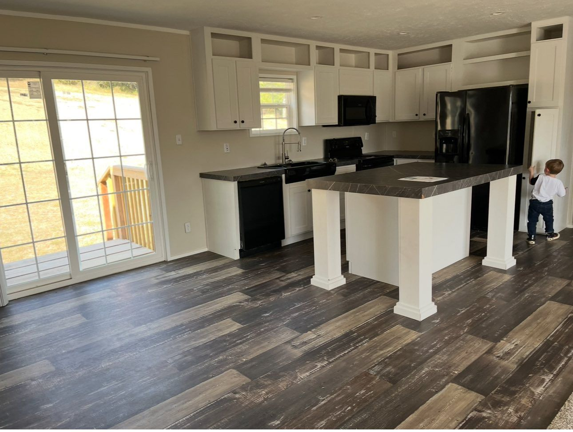 A kitchen with white cabinets, dark countertops, wood-look flooring, a black refrigerator, and a sliding glass door.