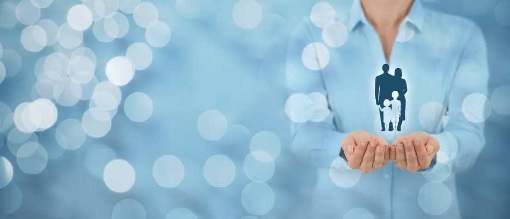 Person holding a family silhouette symbol in cupped hands, against a blue bokeh background.