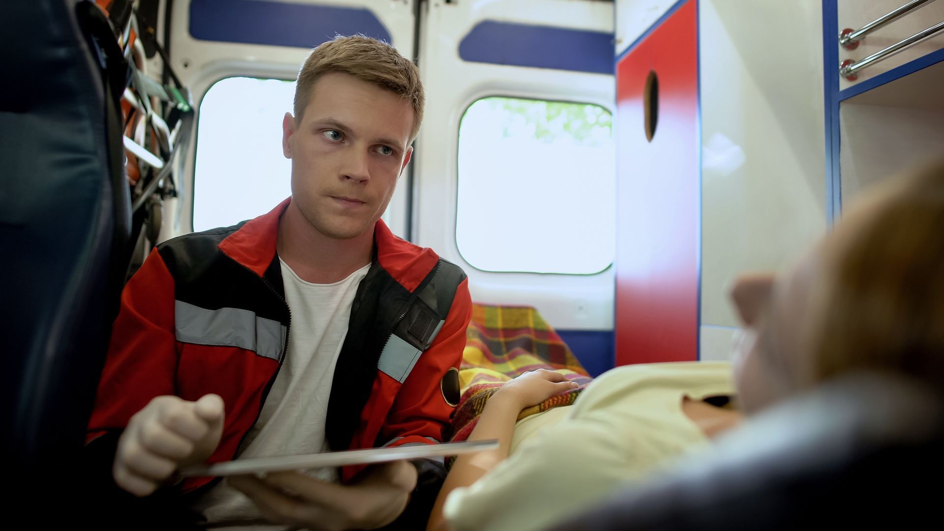 Paramedic monitoring a patient inside an ambulance during emergency transport.