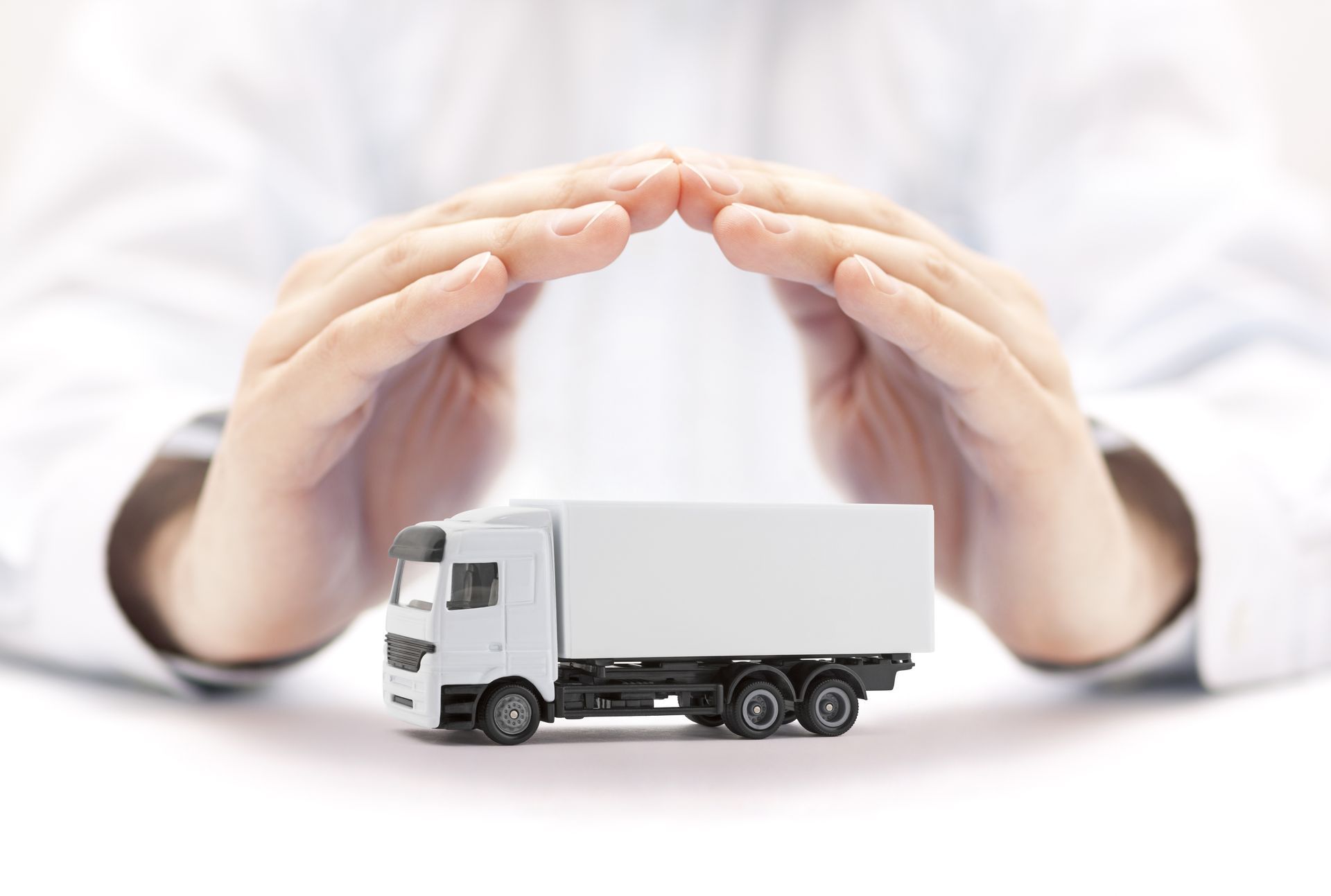 Hands protecting toy truck symbolizing commercial fleet and cargo transport insurance coverage.