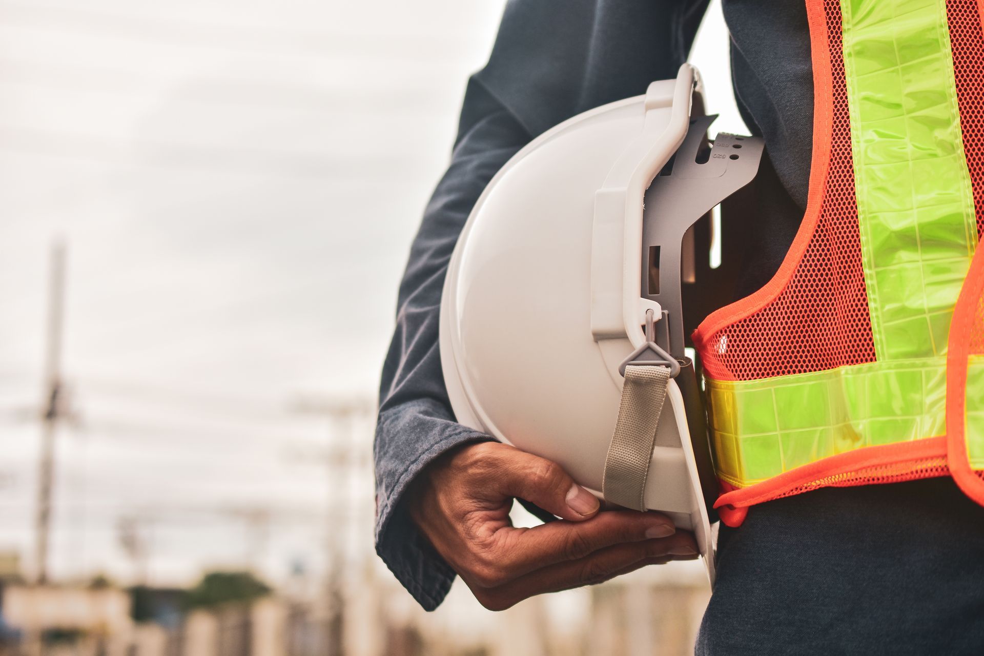 Construction worker holding a white hard hat, wearing a neon safety vest at a job site Construction worker holding a white hard hat, wearing a neon safety vest at a job site