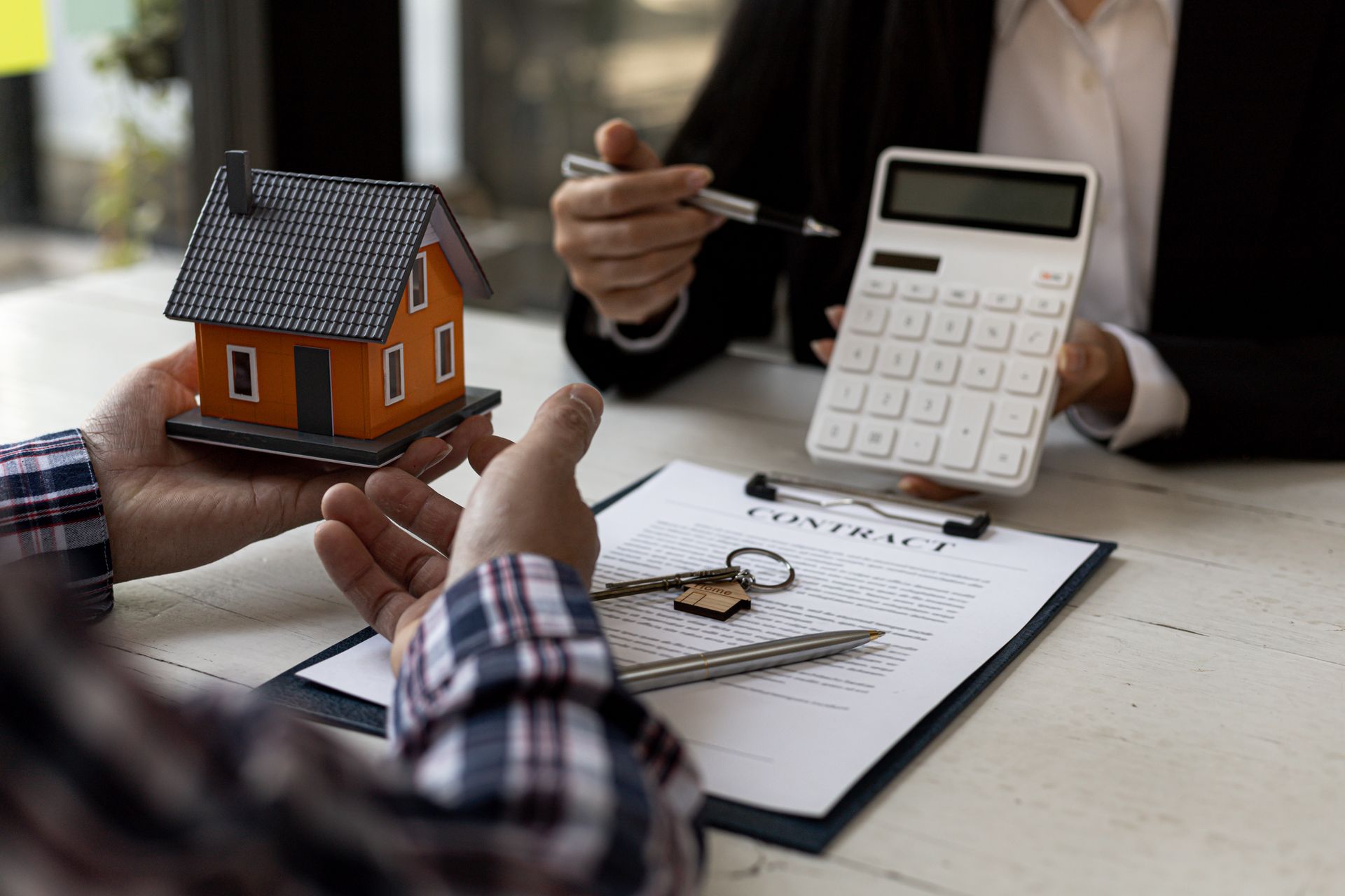 Person discussing home purchase with agent, calculator and house model on table