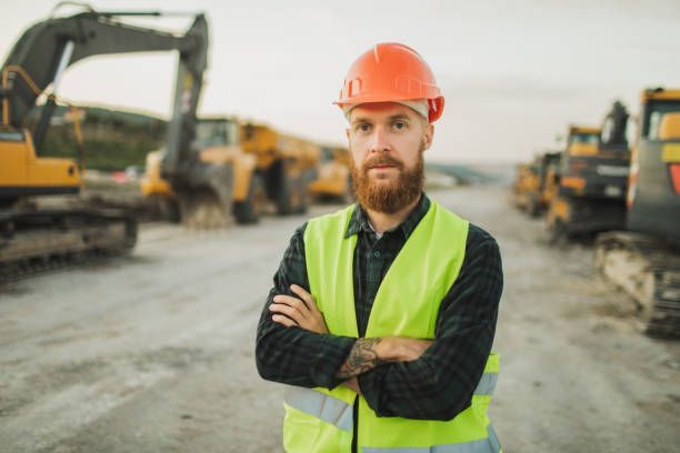 Portrait of a contractor with a helmet on a construction site. Industrial trucks are behind him.