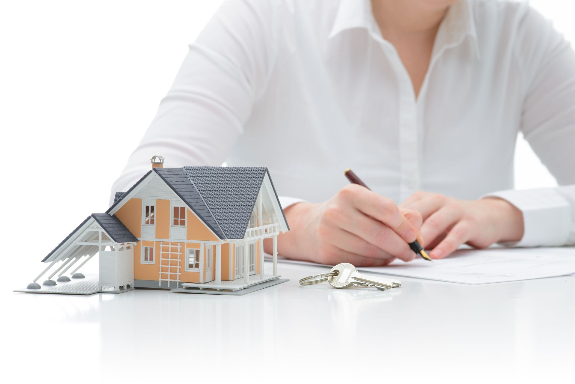 Person signs document next to miniature house and keys, representing contractors insurance.