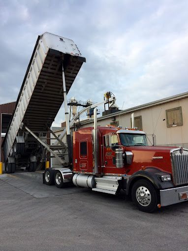 Red GFI Transport semi-truck with dump trailer unloading road salt next to a building.
