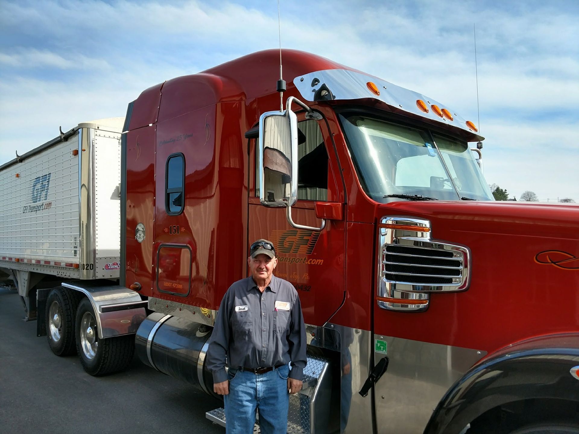 Red semi-truck with trailer parked outdoors, with a worker standing beside it
