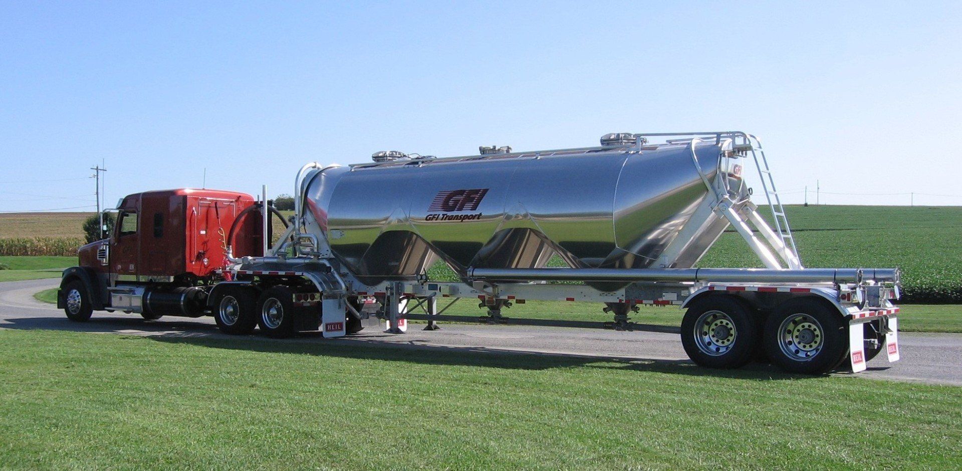 a semi truck with a pneumatic trailer attached to it is parked in a grassy field by GFI Transport in central Pennsylvania