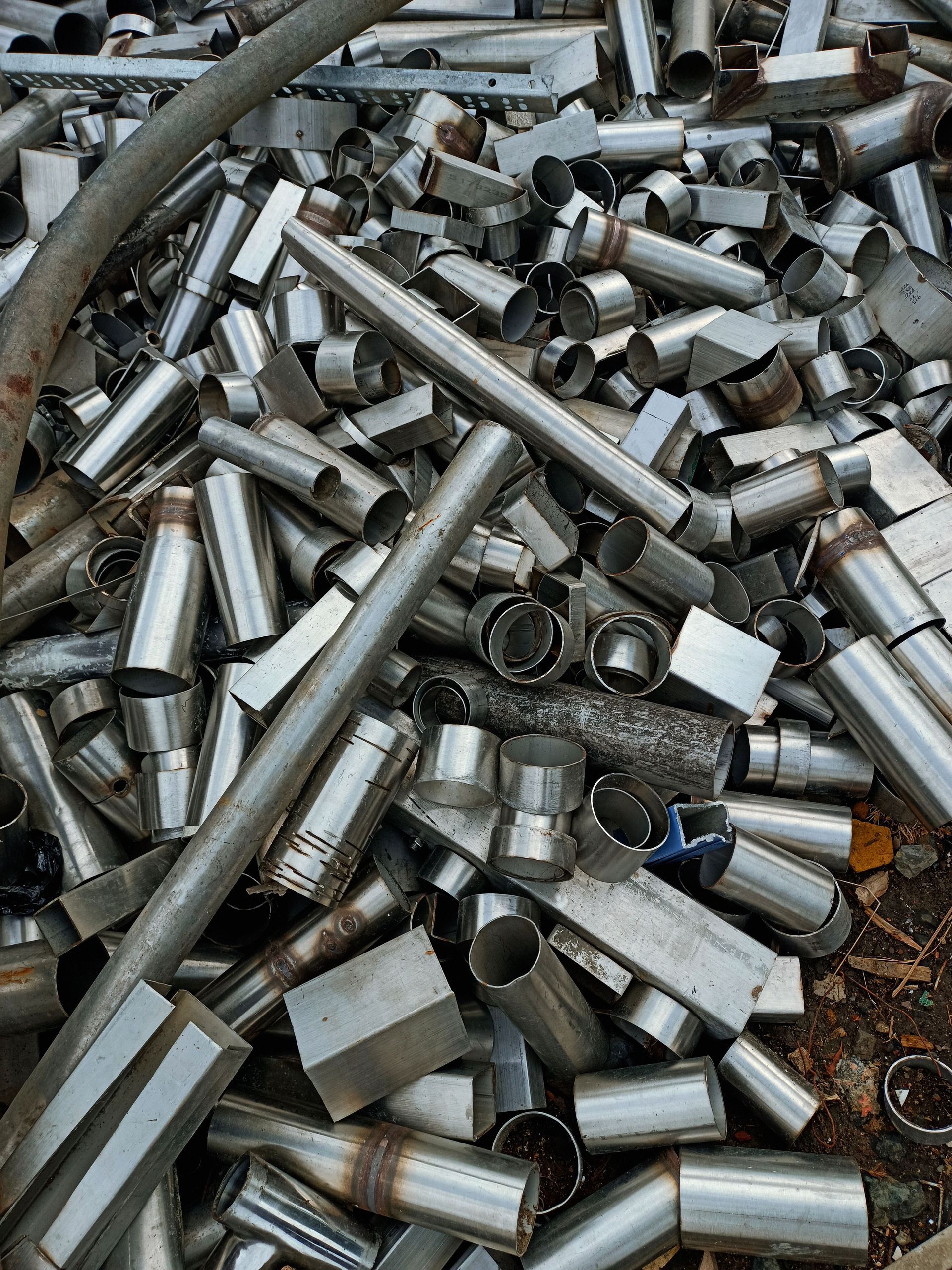 Pile of shiny metal pipe fittings and cut tubes scattered on the ground
