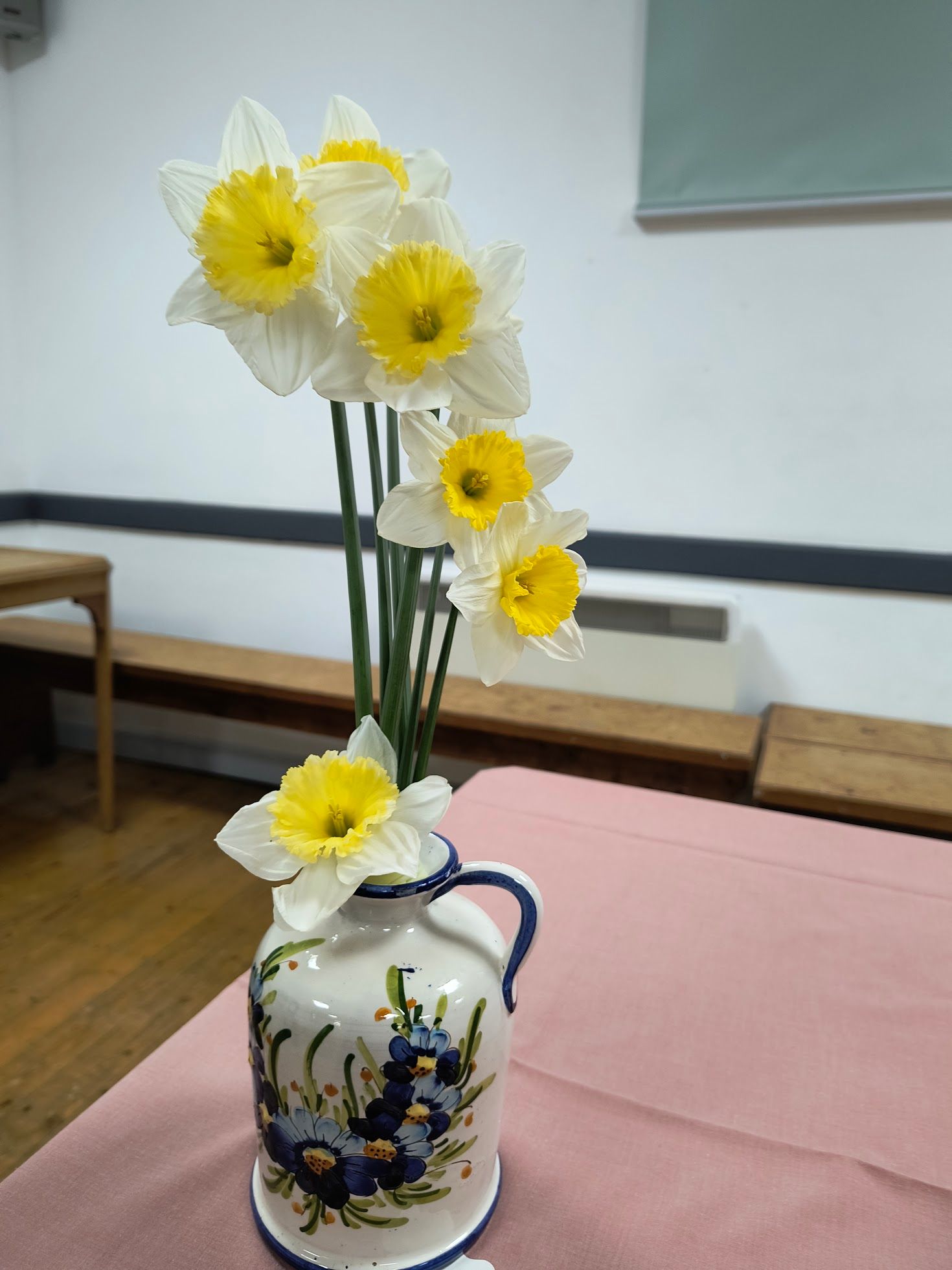 Photo shows an arrangement of deep yellow daffodils and various foliage in a ceramic vase