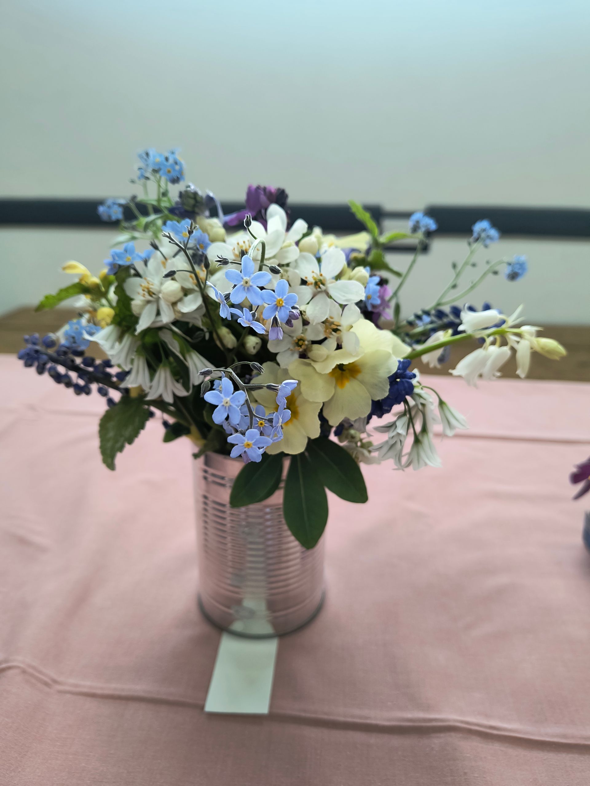 Photo shows a Covid testing box with the plastic tubes positioned in holes in the lid and each containing a small flower (left to right: purple, white, yellow, purple)