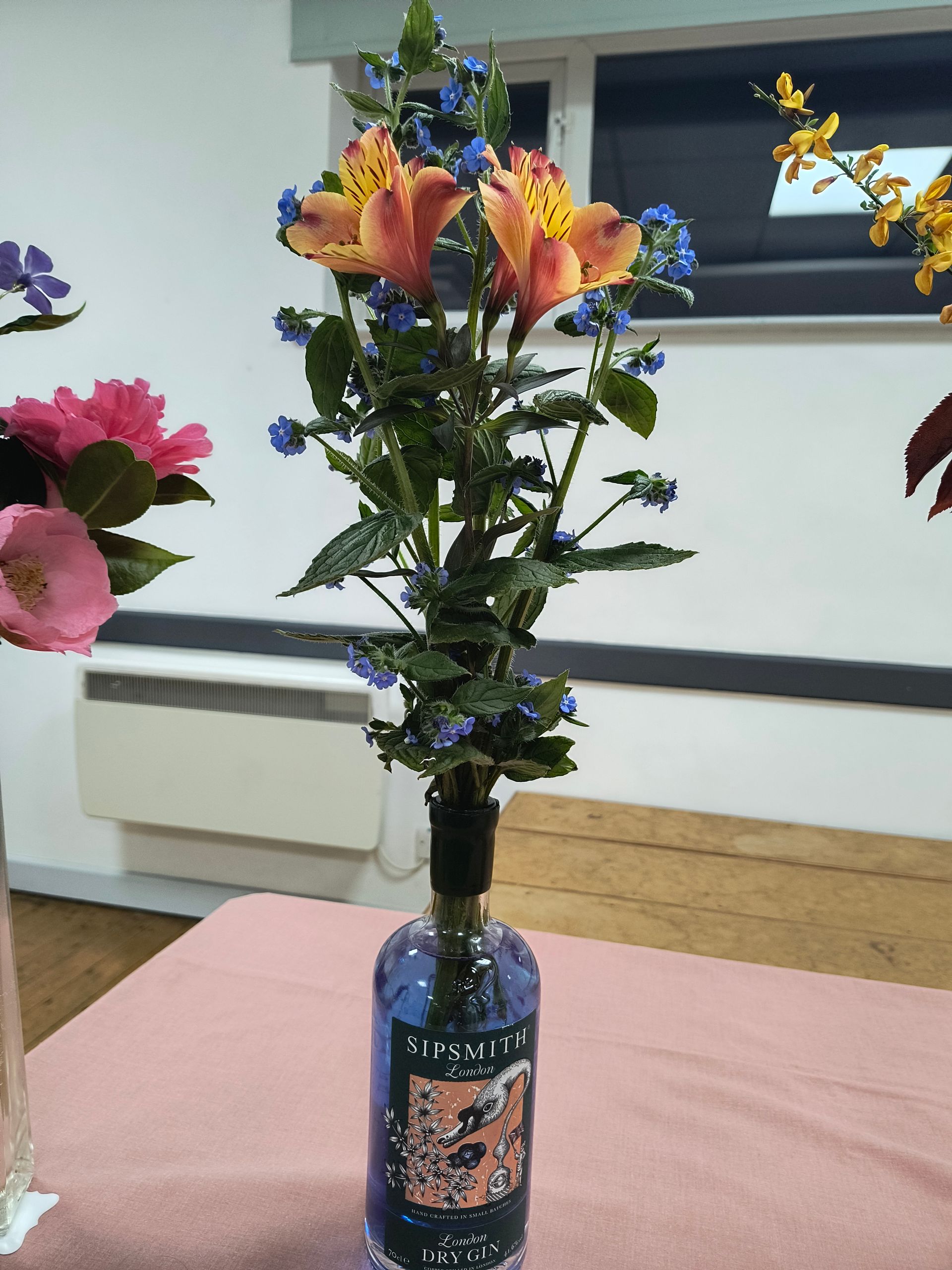 Photo shows a blue Sipsmith Dry Gin bottle holding an arrangement of 2 orange alstromeria and some blue flowers