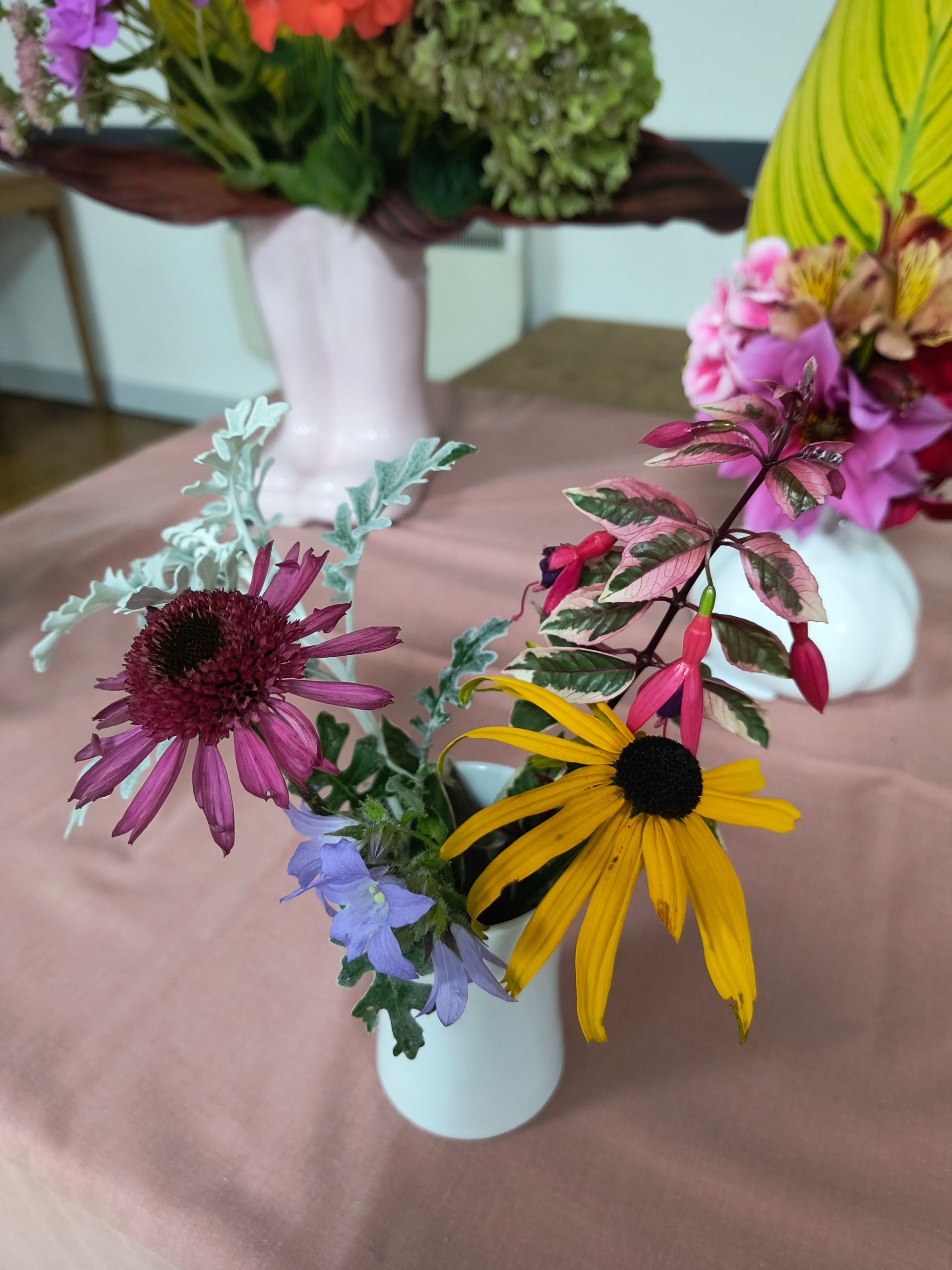 Photo shows pink and orange flowers with foliage in a white vase
