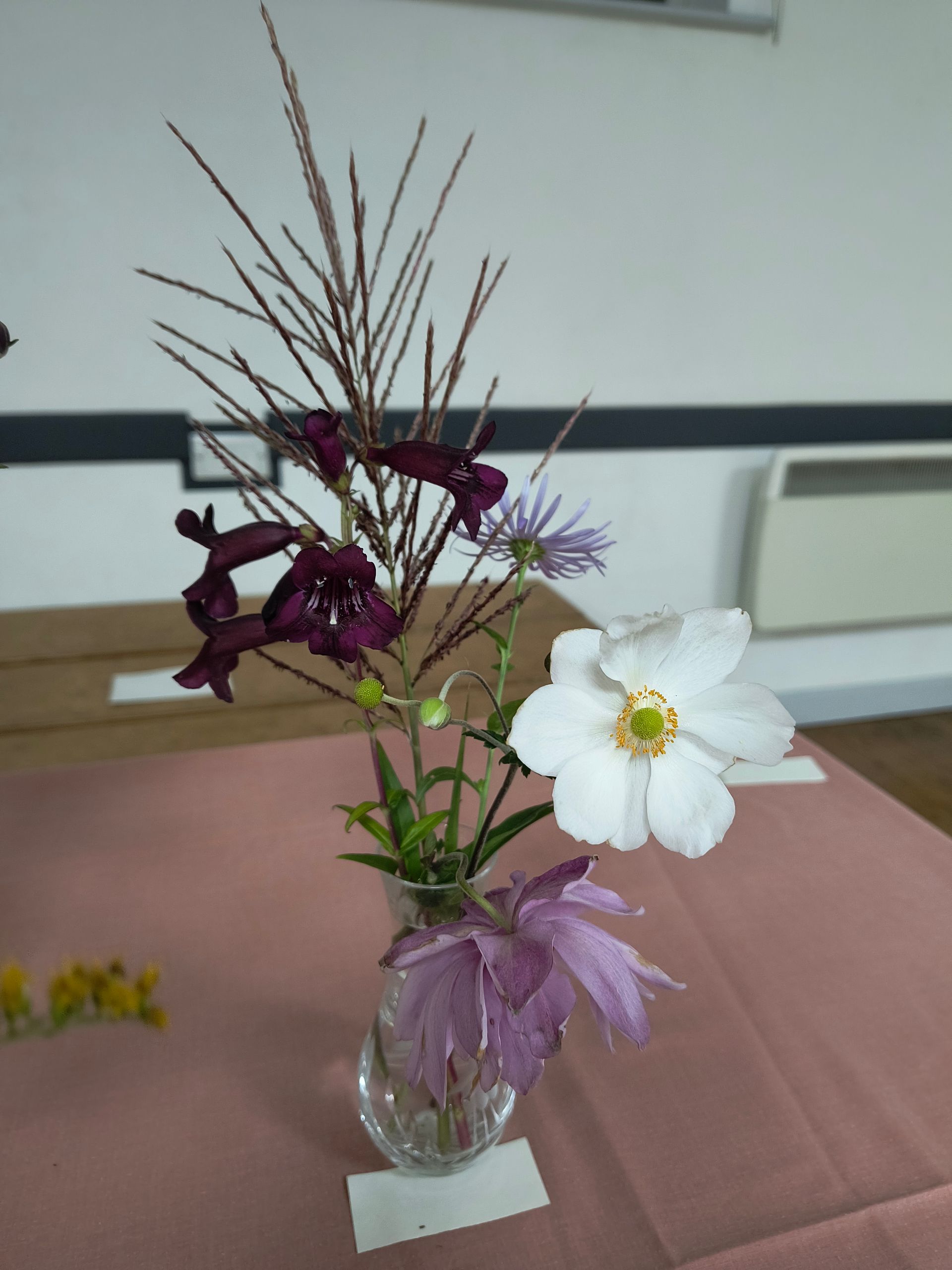 Photo shows purple, pink and white flowers with foliage in a glass vase