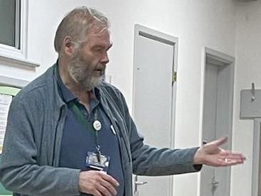 Photo shows Chris Bird at front of Hall answering questions from Members