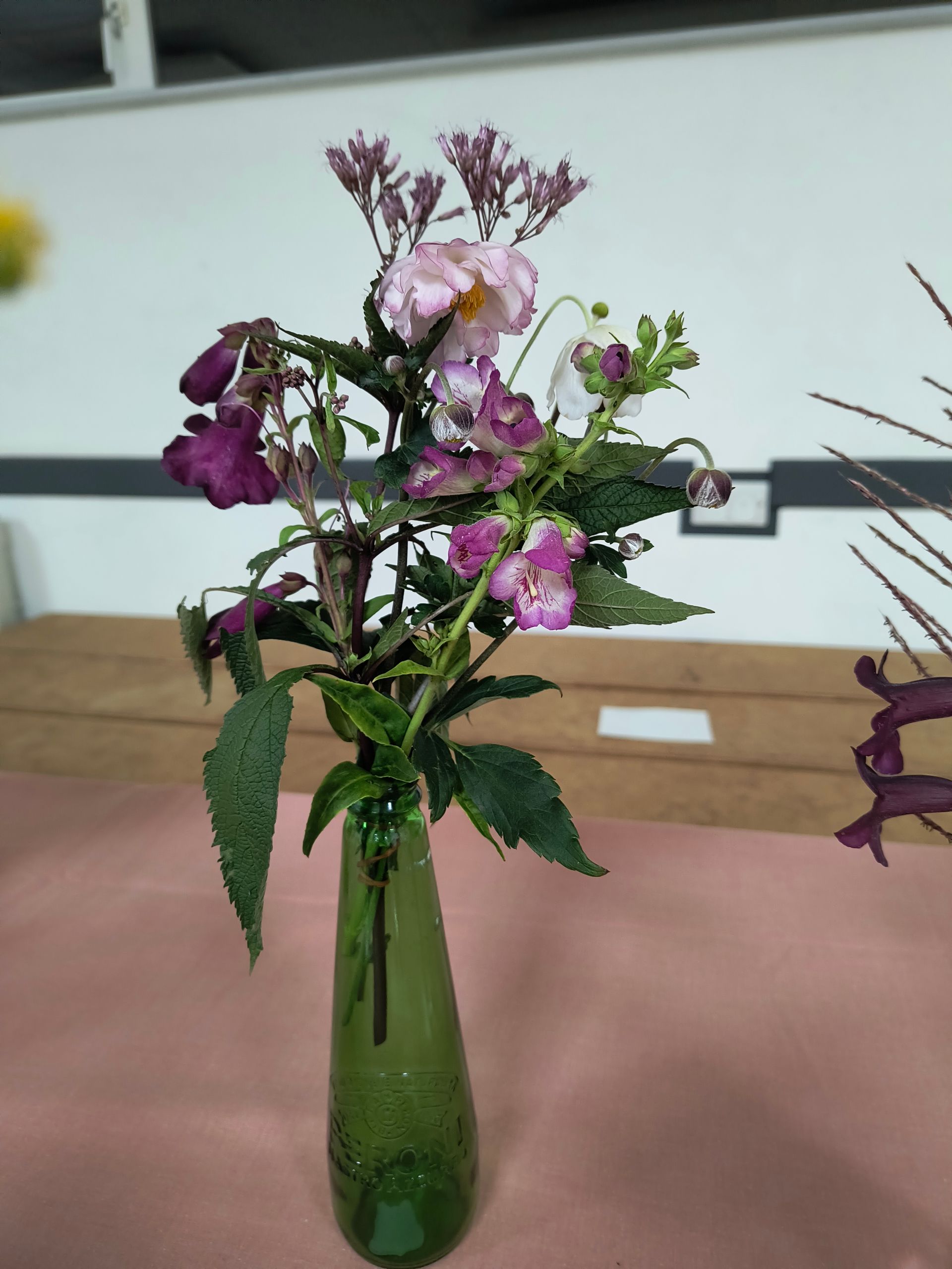 Photo shows purple flowers and foliage in a green glass vase