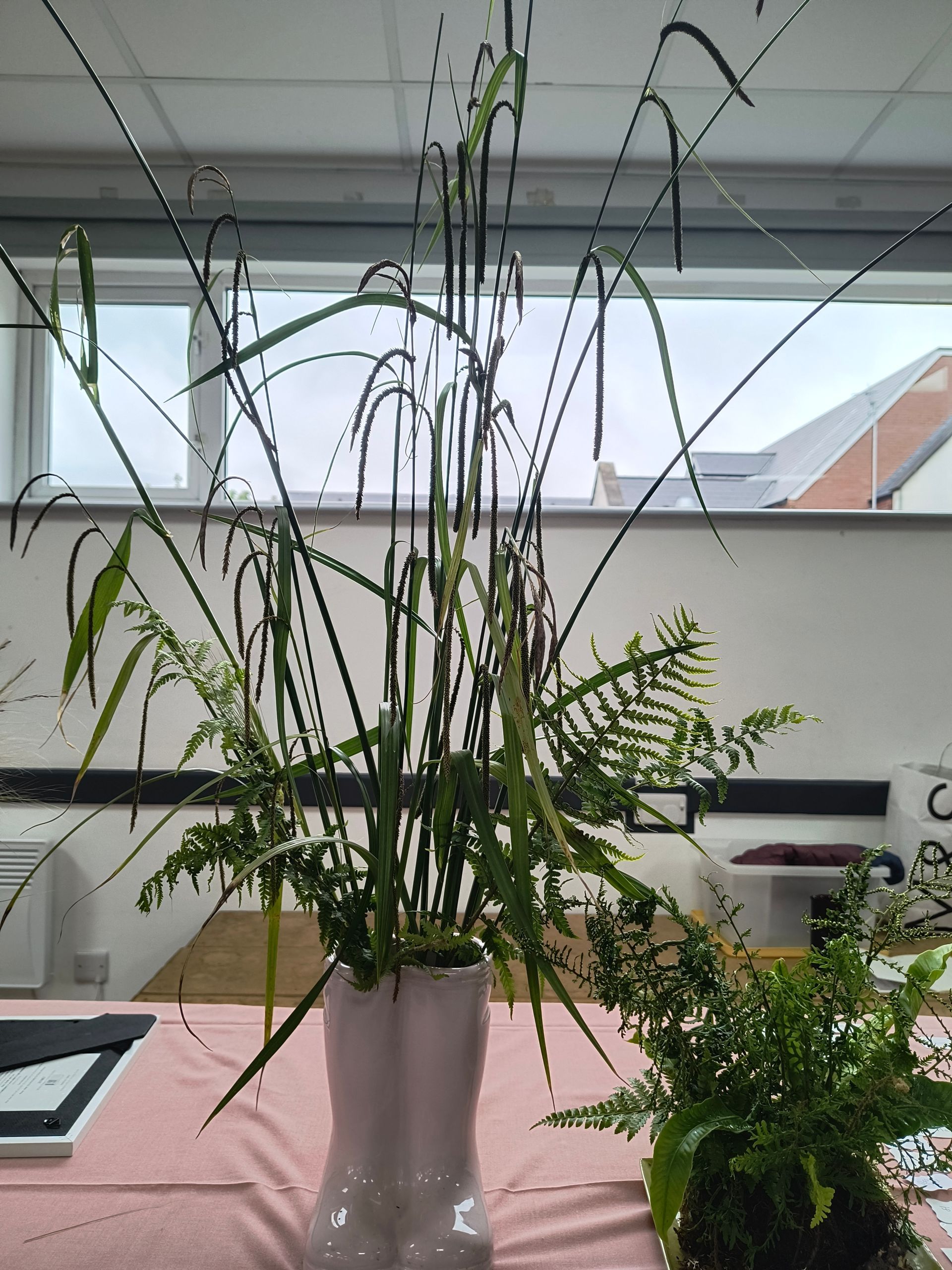 An arrangement of tall grasses and ferns in a vase styled as two wellington boots