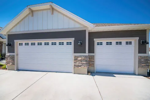 Home exterior with white double garage doors with windows and half stone walls 