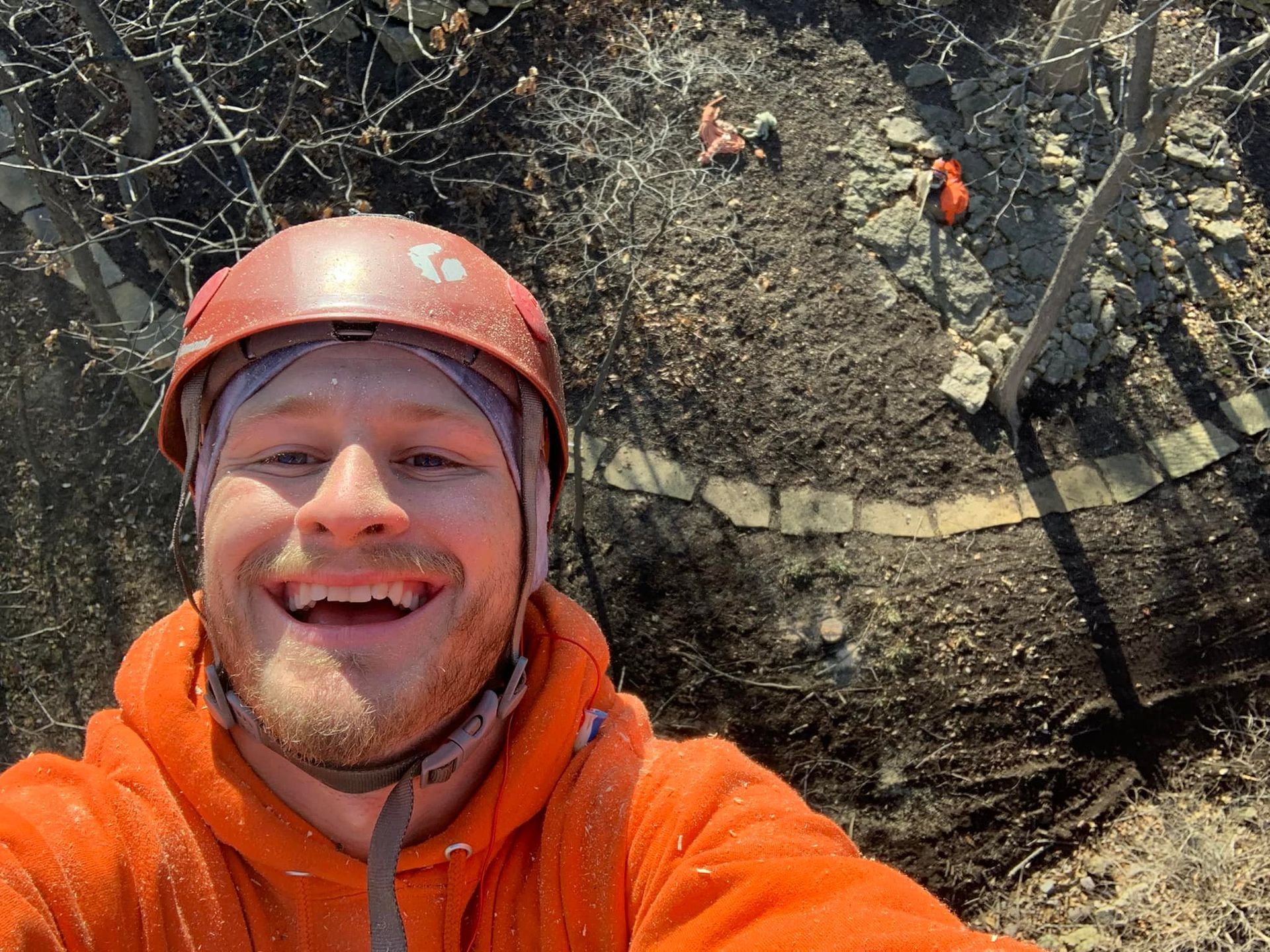 Smiling person in orange hoodie and helmet, rock climbing. Other people working above. Smiling person in orange hoodie and helmet, rock climbing. Other people working above.