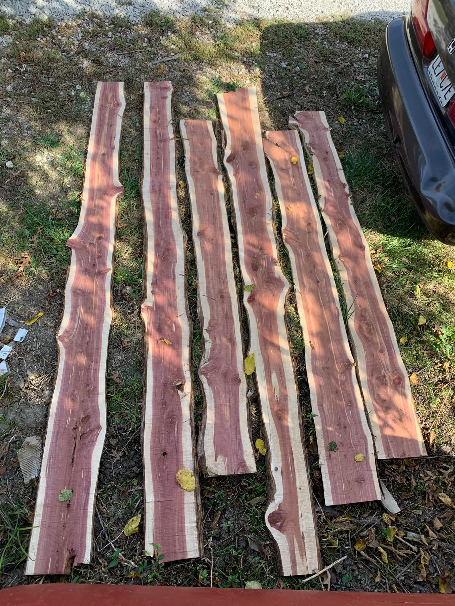 Seven reddish-brown cedar planks with live edges, lying on a surface with scattered leaves. Seven reddish-brown cedar planks with live edges, lying on a surface with scattered leaves.
