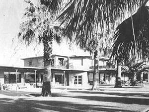 A black and white photo of a house with palm trees in front of it.