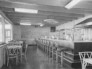 A black and white photo of a restaurant with tables and chairs and a bar.