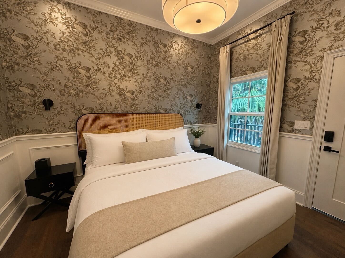 Elegant bedroom with floral wallpaper, white bedding, and a window with daylight.