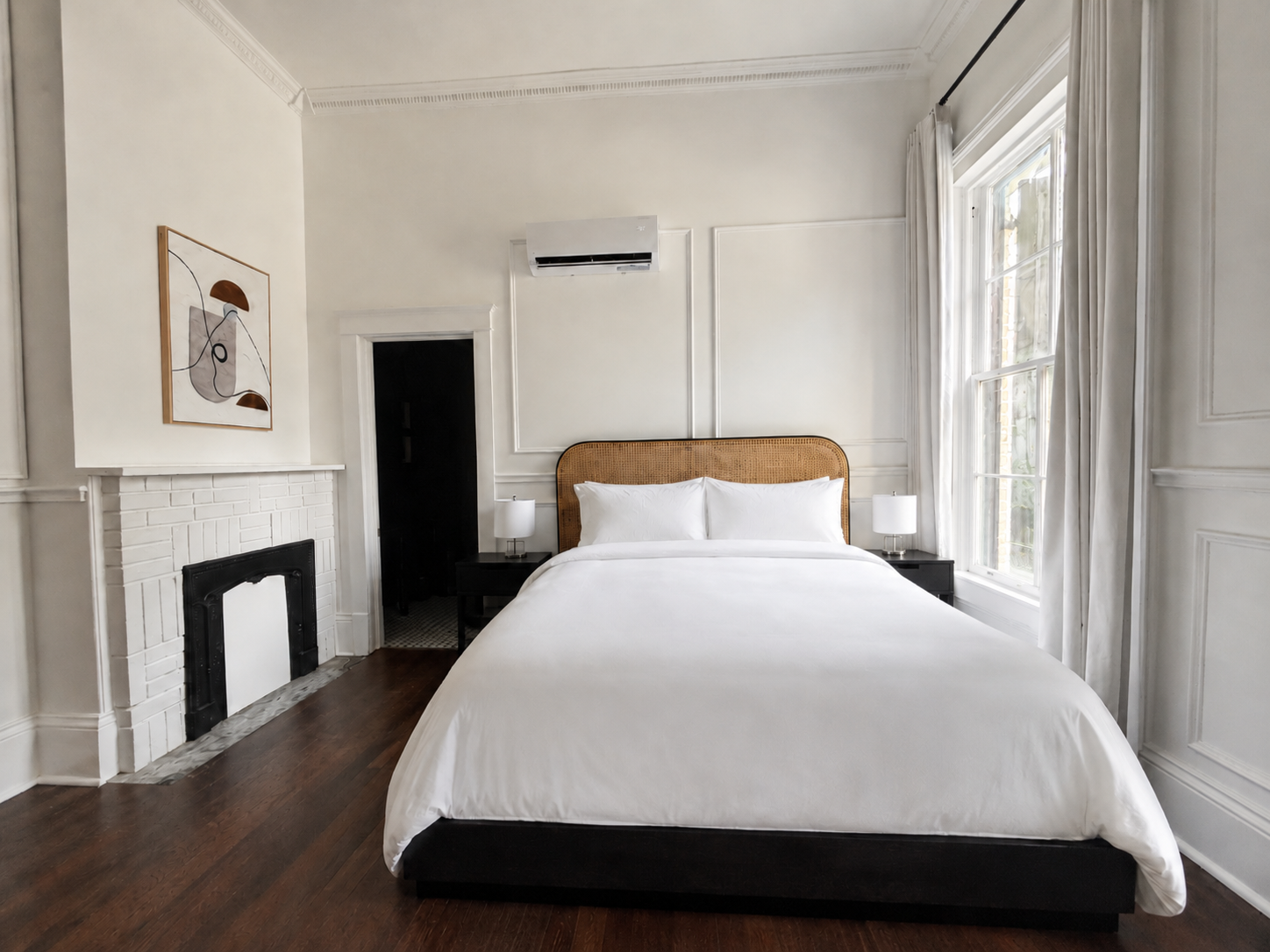 Bright bedroom with a bed, fireplace, and tall windows in a white room