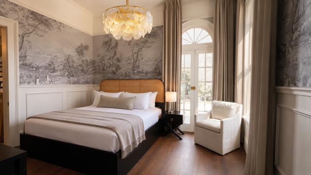 Elegant bedroom with a bed, white armchair, chandelier, and large window with curtains