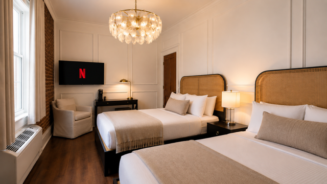 Elegant hotel room with two beds, chandelier, armchair, desk, and wall-mounted TV