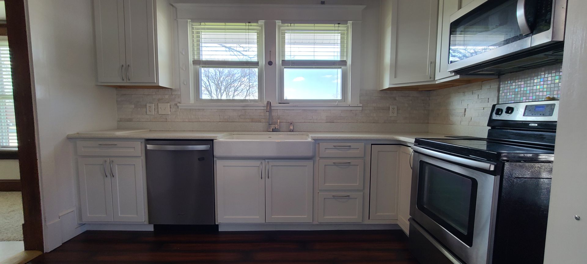 An empty kitchen with white cabinets , a stove , dishwasher , and microwave.