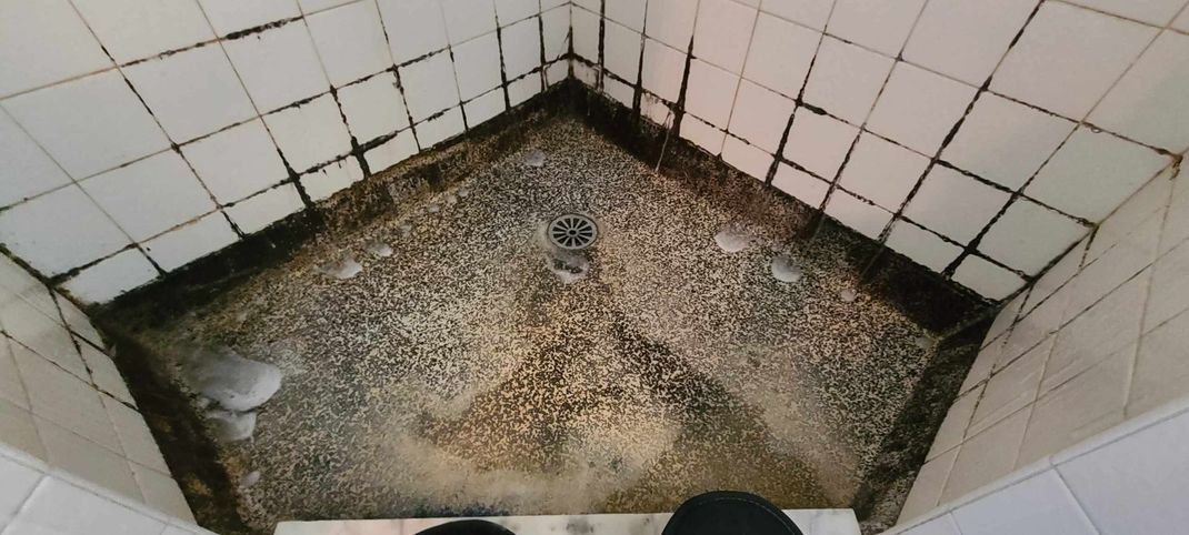 A person is standing in a bathroom with a dirty floor.