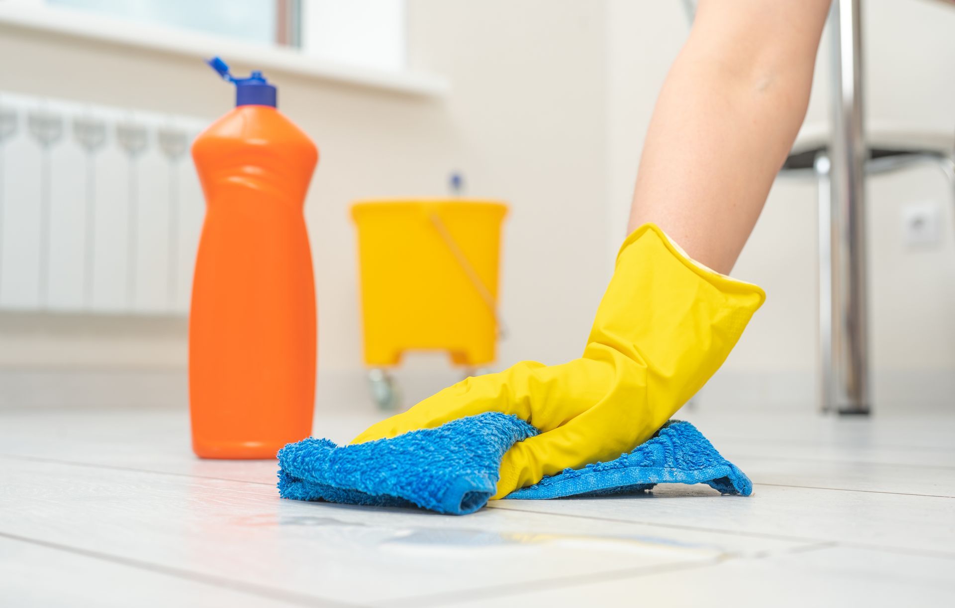 A person wearing yellow gloves is cleaning the floor with a blue cloth.