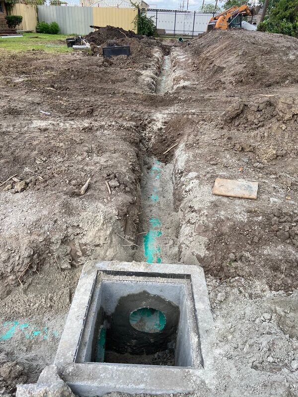 Open trench with a concrete utility box and green pipe at a construction site.